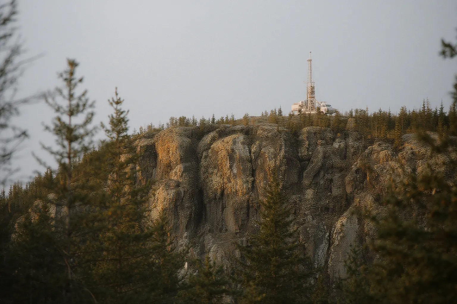 Small drilling rig with a slim mast on a distant rocky forested ridge